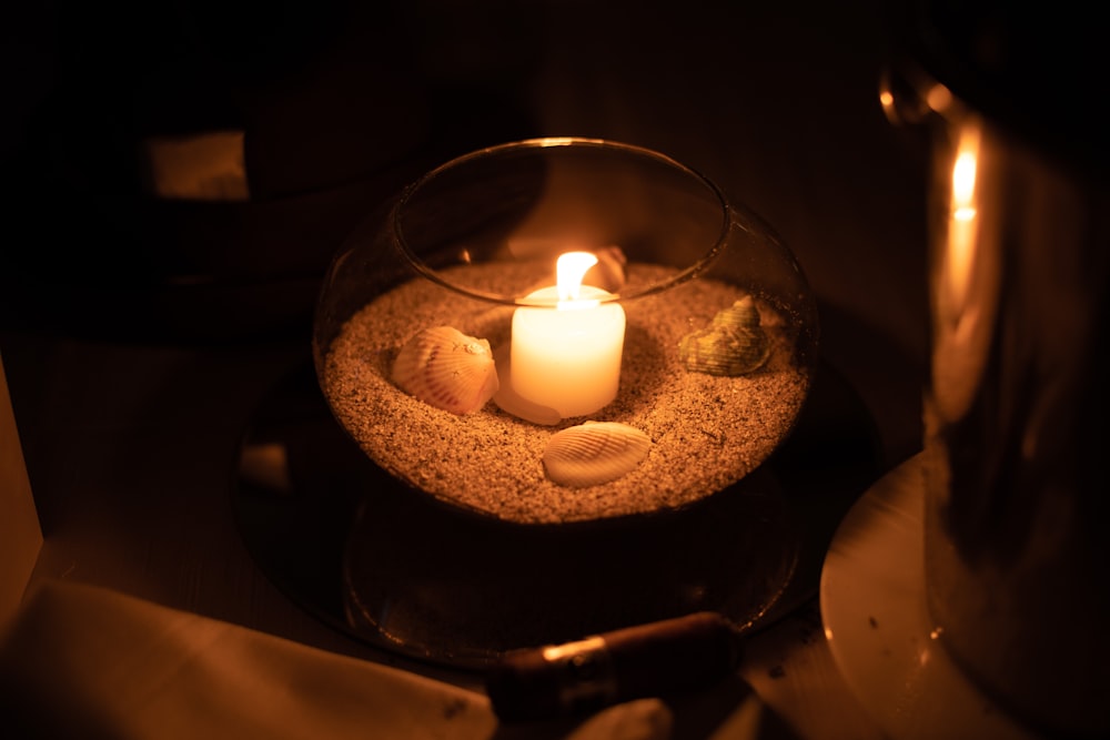 eine brennende Kerze in einer mit Sand und Muscheln gefüllten Schale