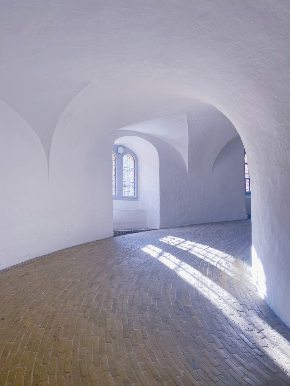 a white room with a brick floor and arched windows