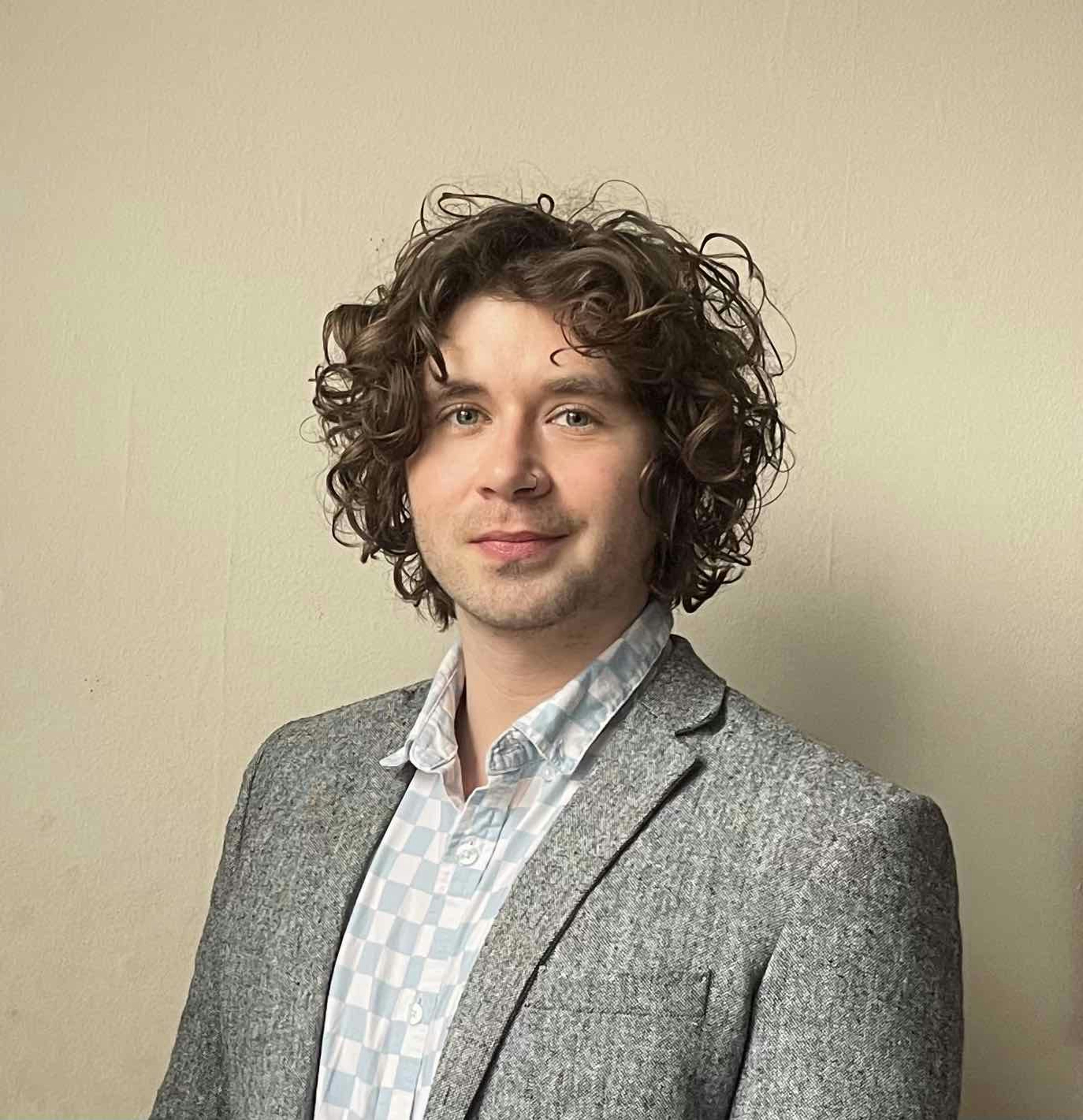 a man with curly hair standing in front of a wall