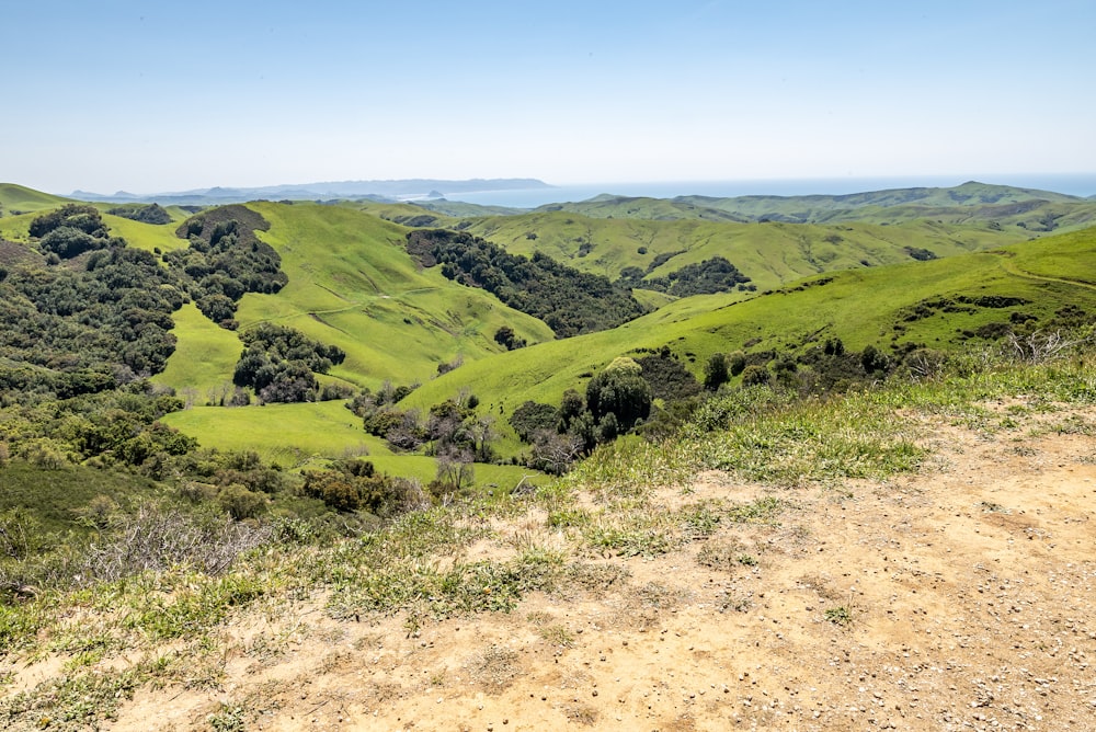 a dirt road on a hill with green hills in the background