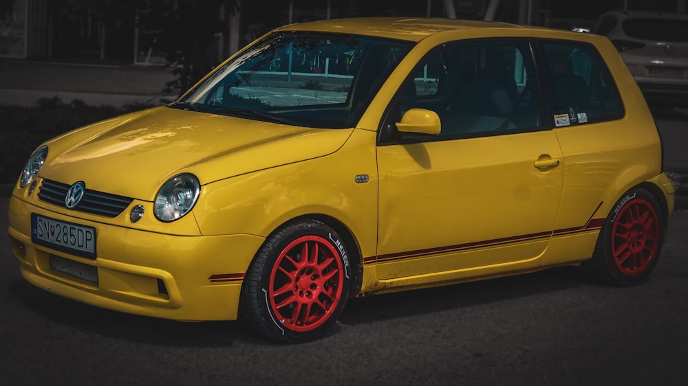 a yellow car with red rims parked in a parking lot