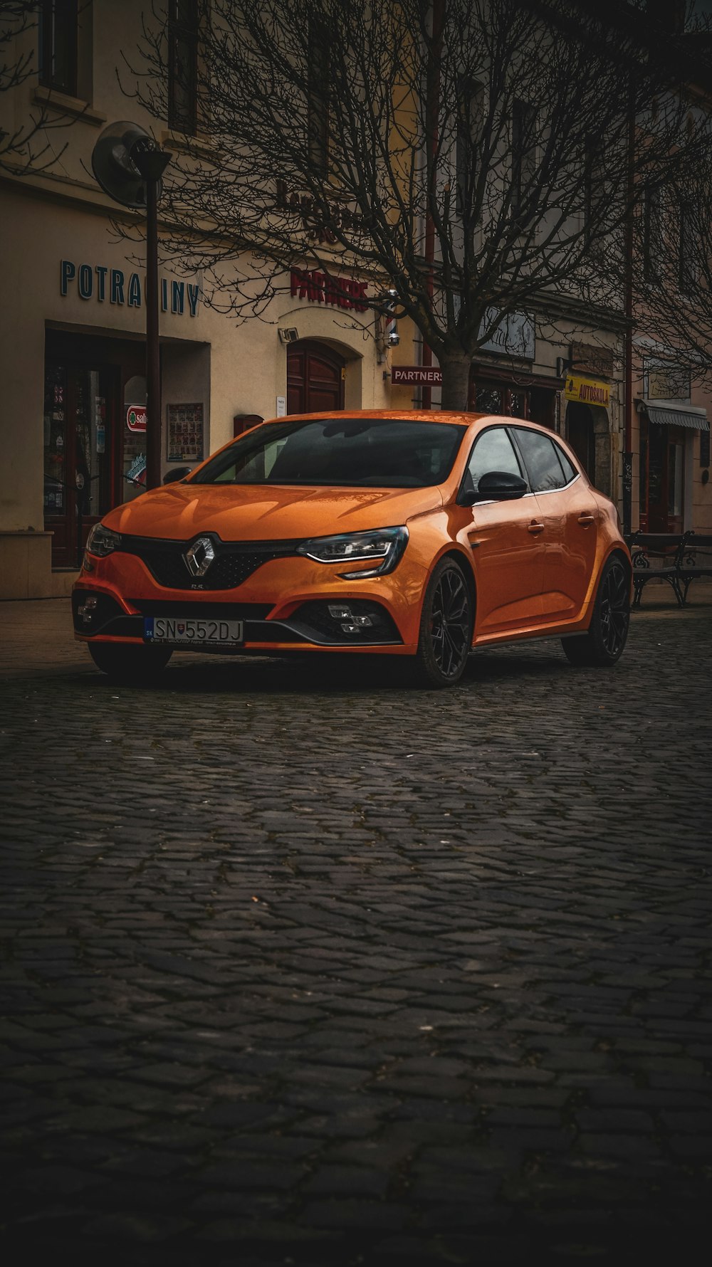 an orange car parked on a cobblestone street