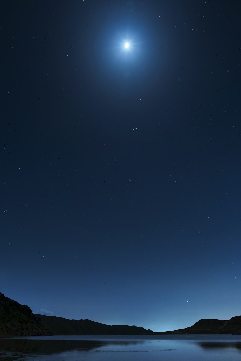 a bright moon shines in the night sky over a lake