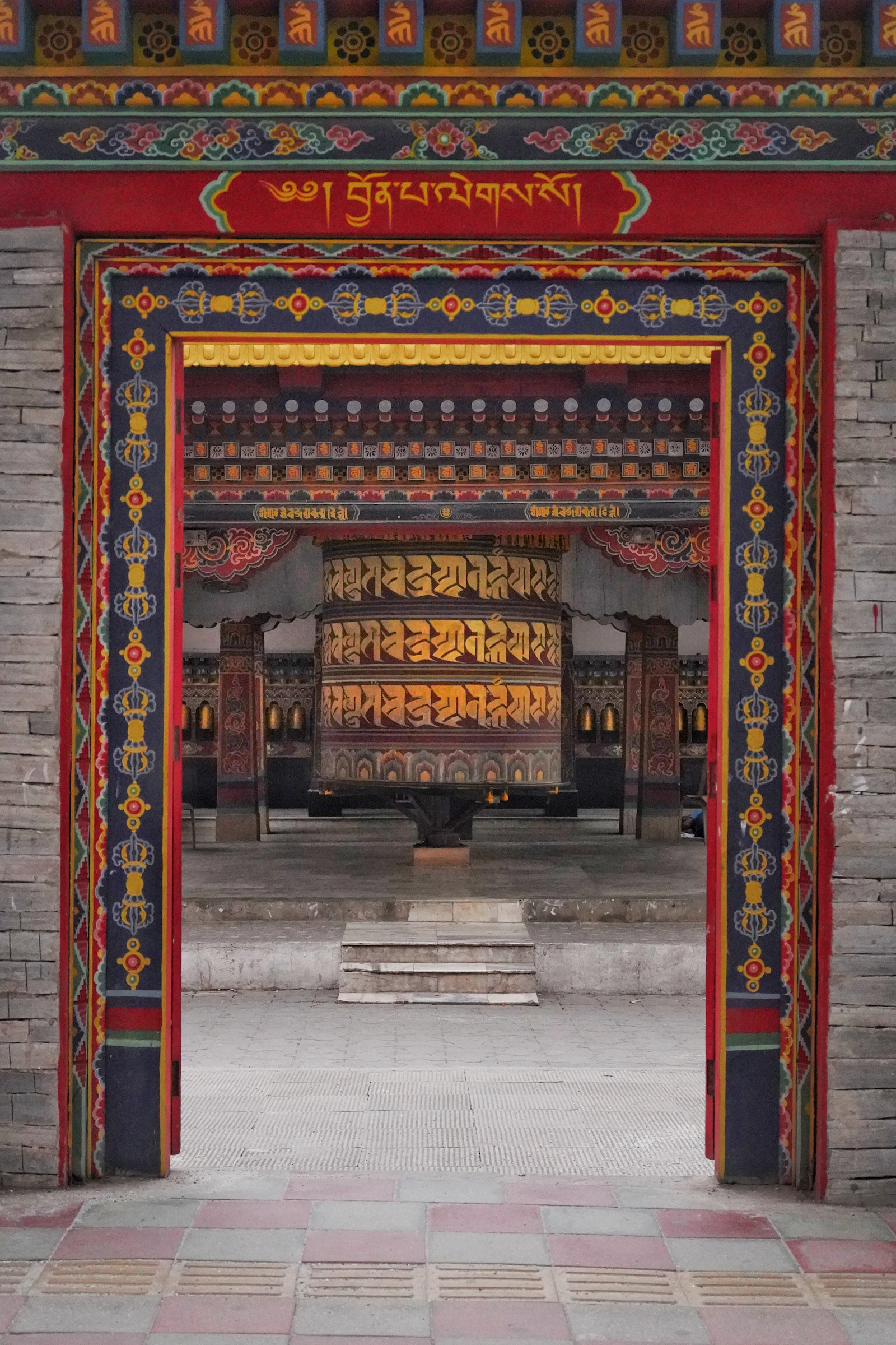 A painted gateway in Phuentsholing opening onto a flagstone court and a great gilded prayer wheel
