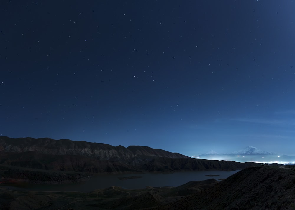 a view of the night sky over a lake and mountains