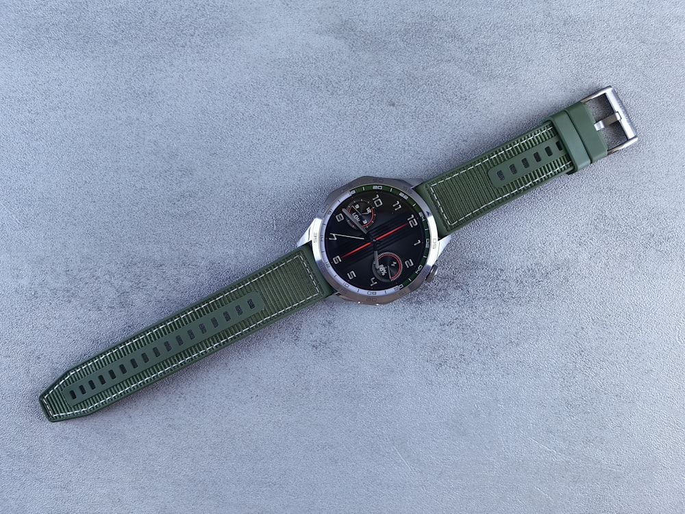a watch with a green strap on a gray surface