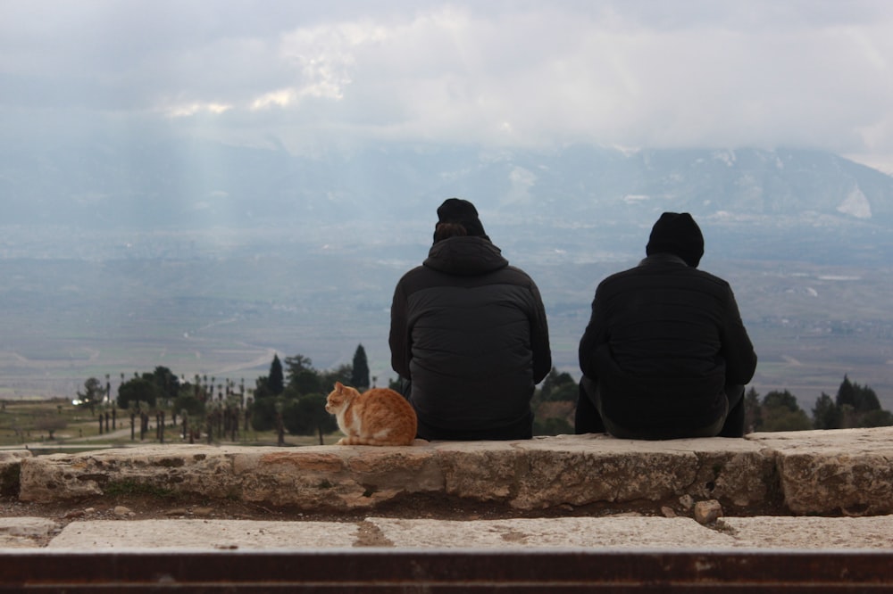 a couple of people sitting on top of a stone wall