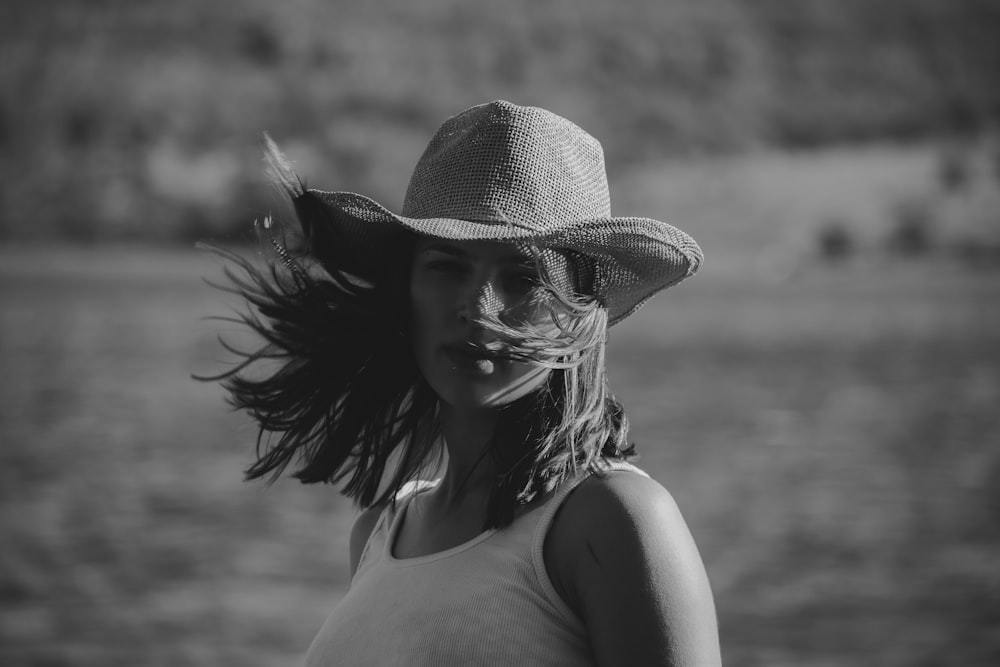 a woman wearing a hat standing in front of a body of water