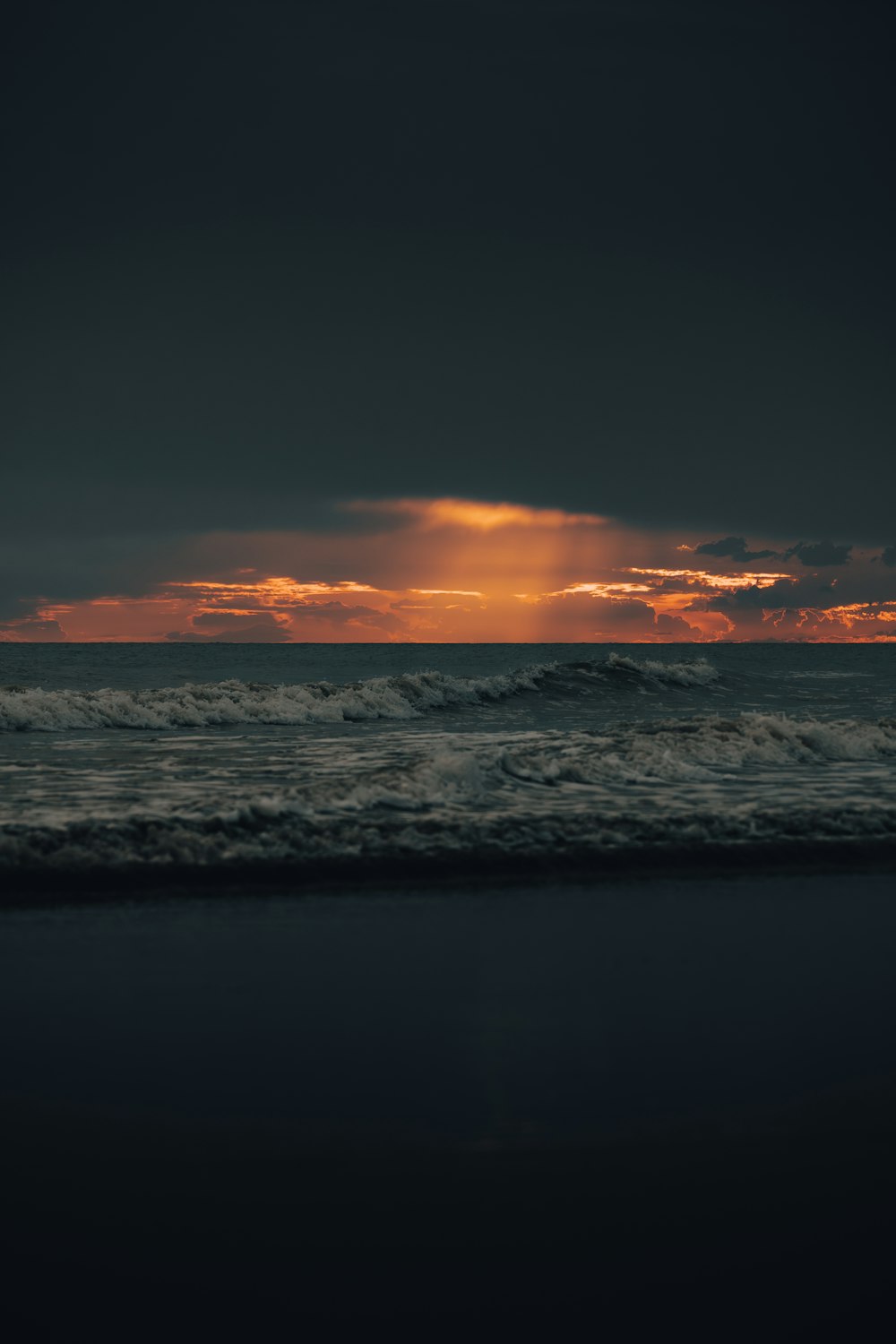 the sun is setting over the ocean on a cloudy day