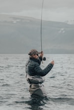 a man standing in the water while holding a fishing rod