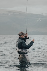a man standing in the water while holding a fishing rod