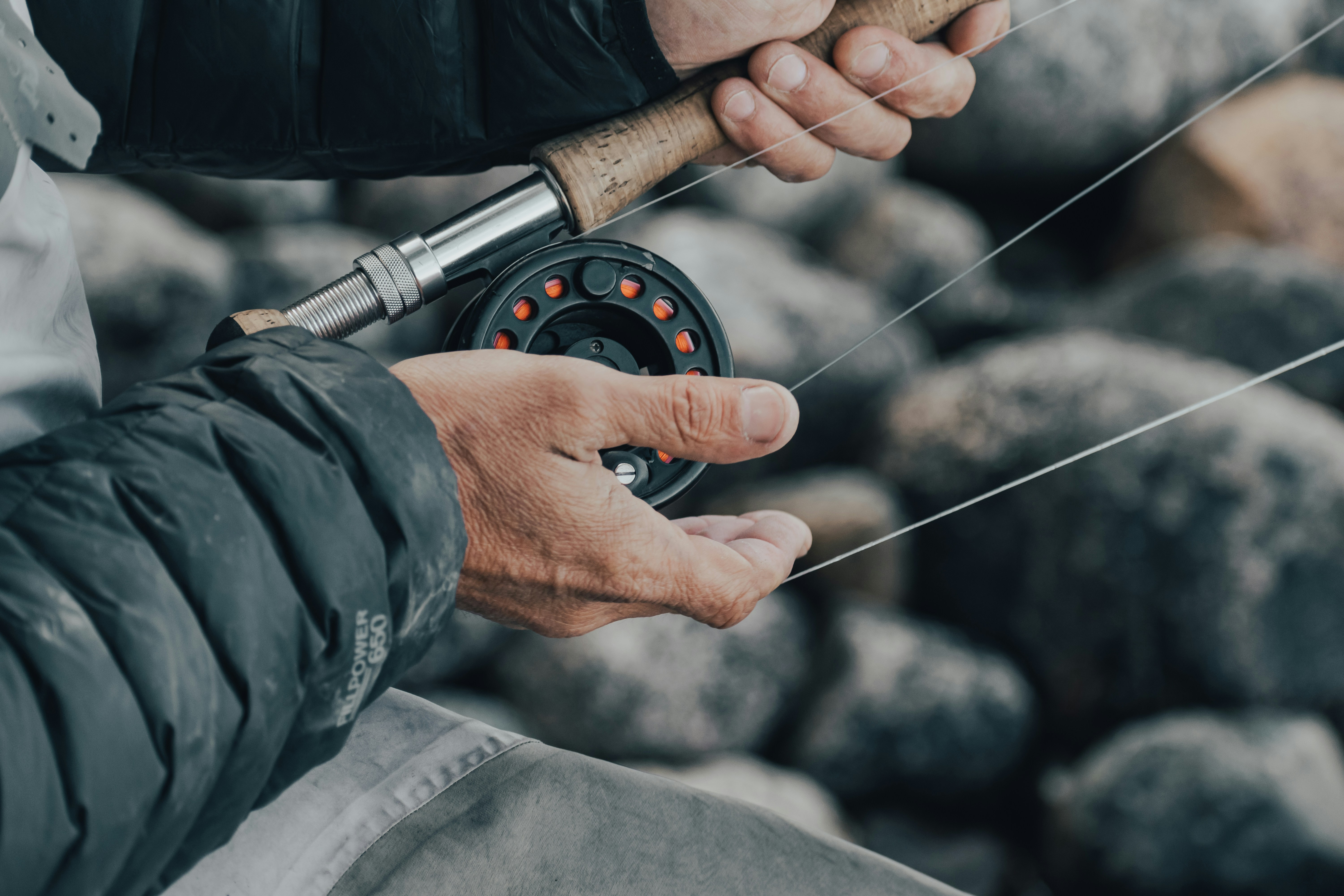 a man holding a fishing rod while sitting on a rock
