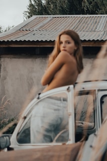 a naked woman leaning on the hood of a car