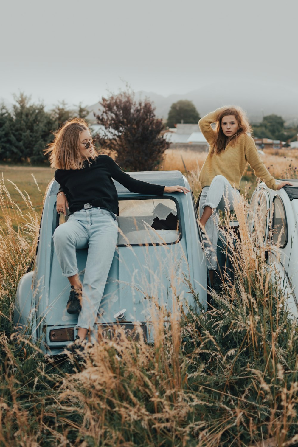 two women sitting on the hood of an old pickup truck