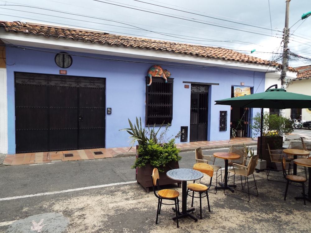 a blue building with tables and chairs and an umbrella