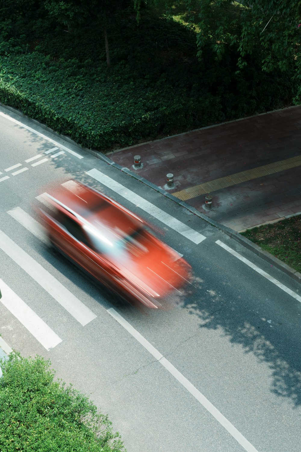 a red car driving down a street next to a lush green hillside