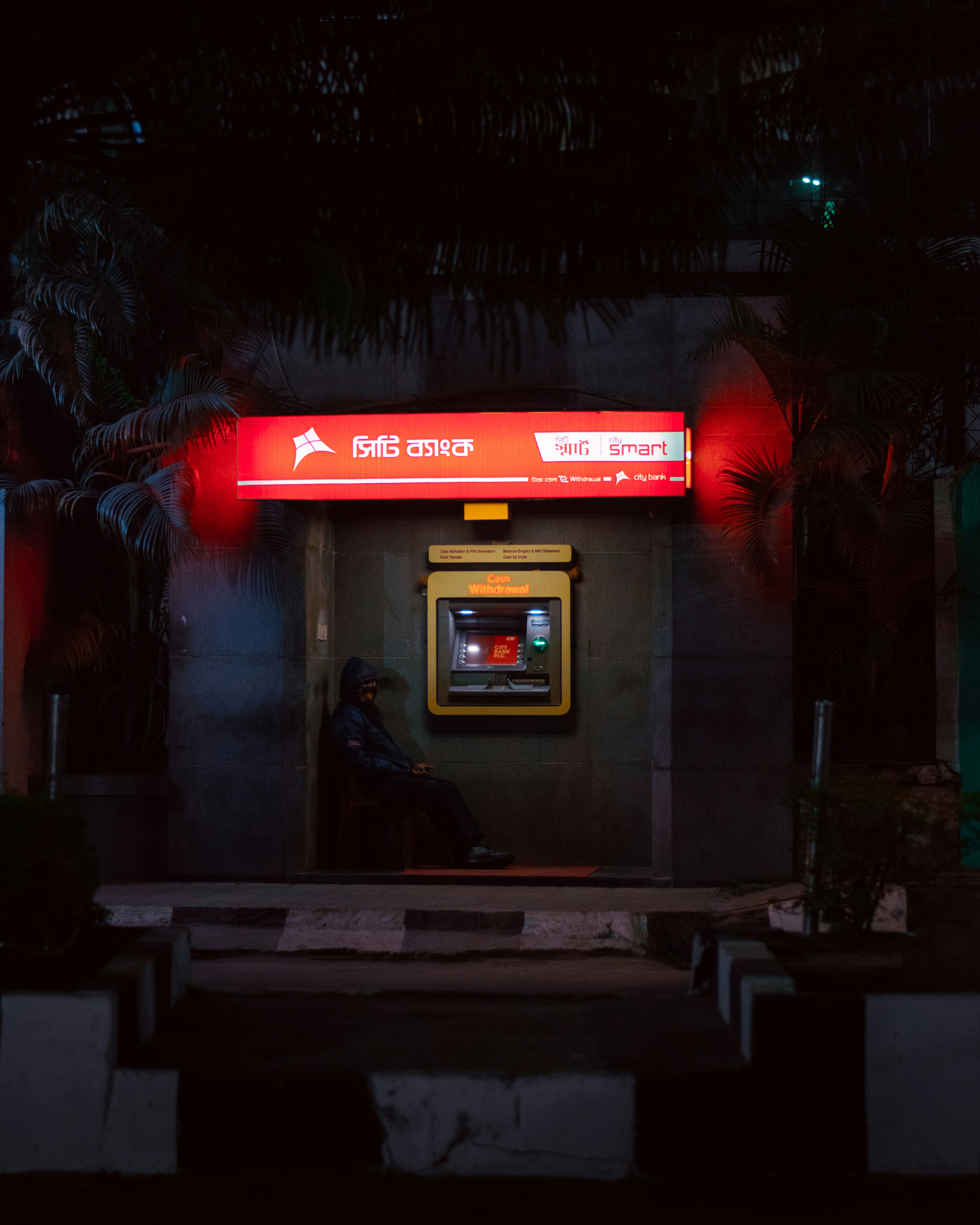um homem sentado em um banco em frente a uma cabine telefônica