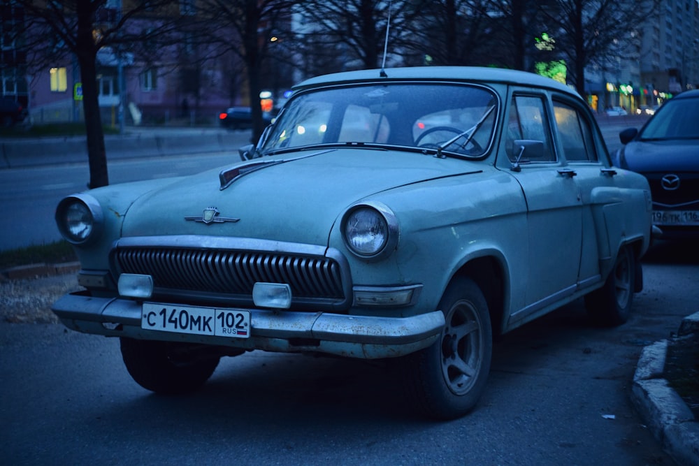 an old blue car parked on the side of the road