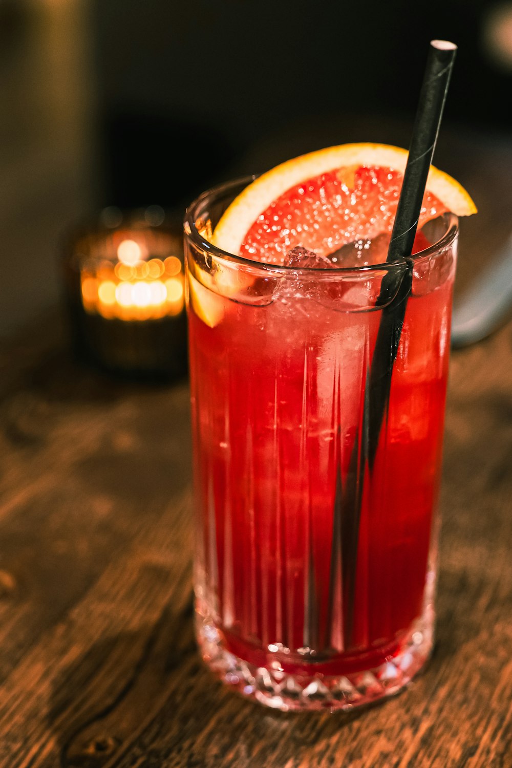 a blood orange drink with a black straw in a glass