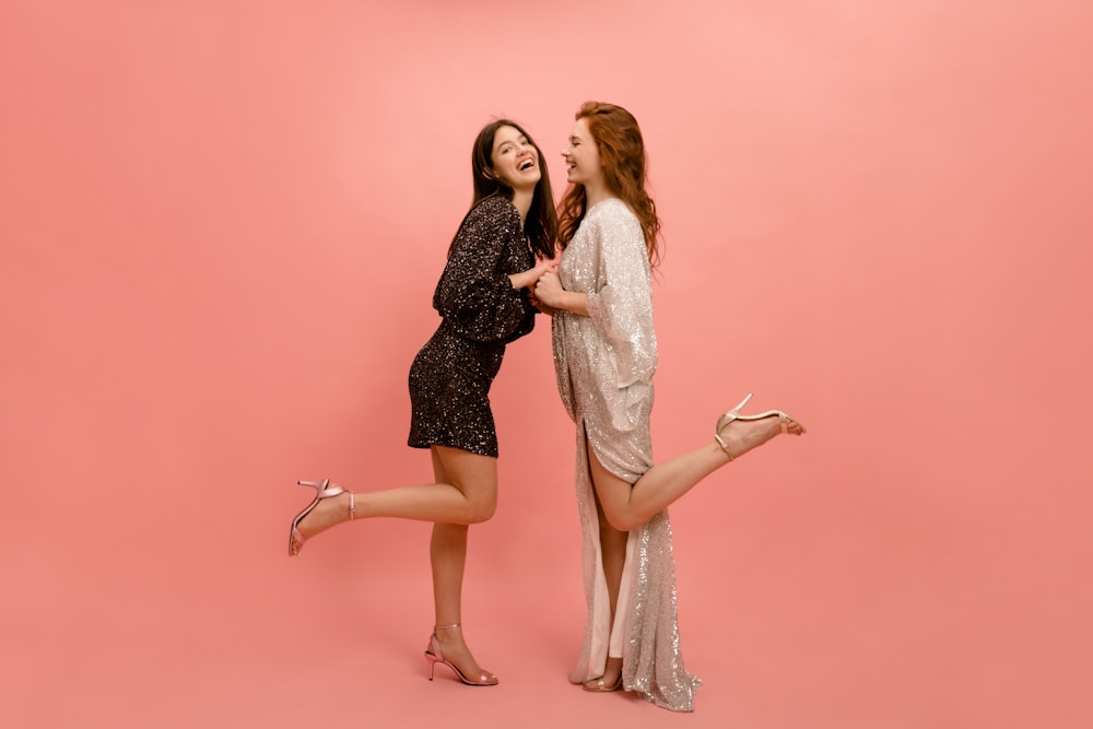 two women standing next to each other on a pink background
