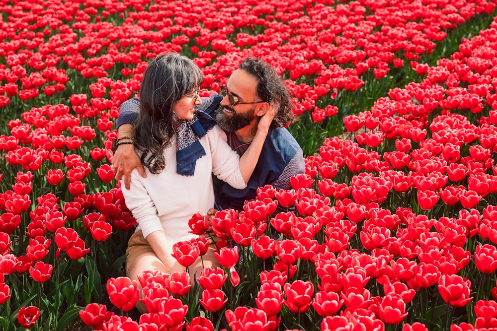 a man and woman sitting in a field of red tulips