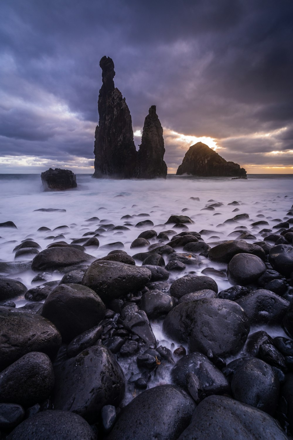 a beach with rocks and water under a cloudy sky