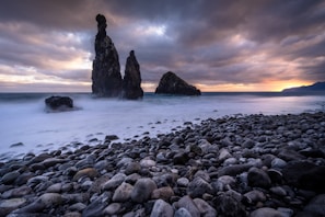 a rocky beach with rocks and water under a cloudy sky