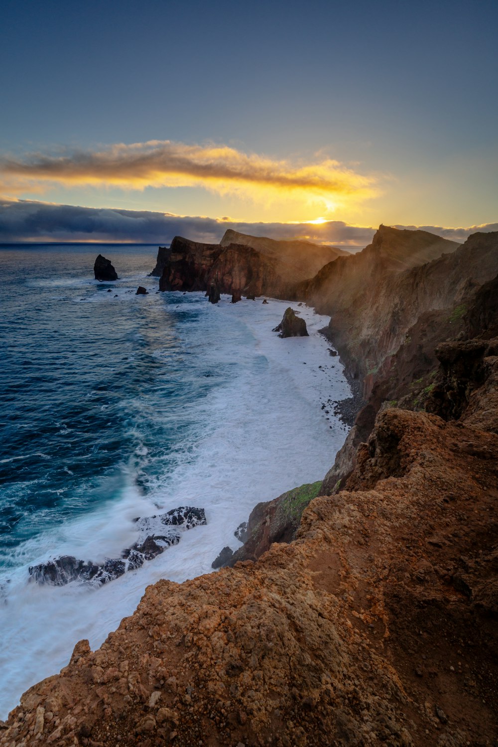 the sun is setting over the ocean near a rocky cliff