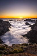 the sun is setting over the clouds in the mountains