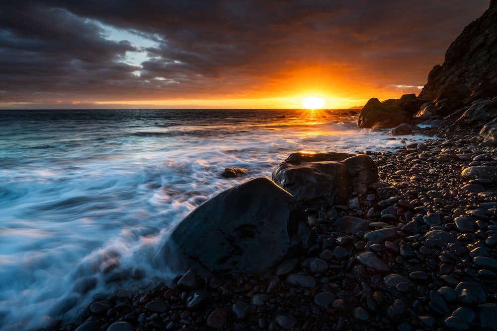 the sun is setting over a rocky beach
