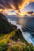 the sun is setting over the ocean on a rocky cliff