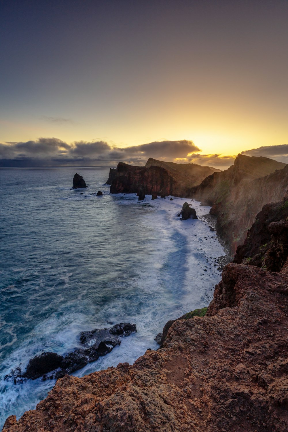 the sun is setting over the ocean near a rocky shore