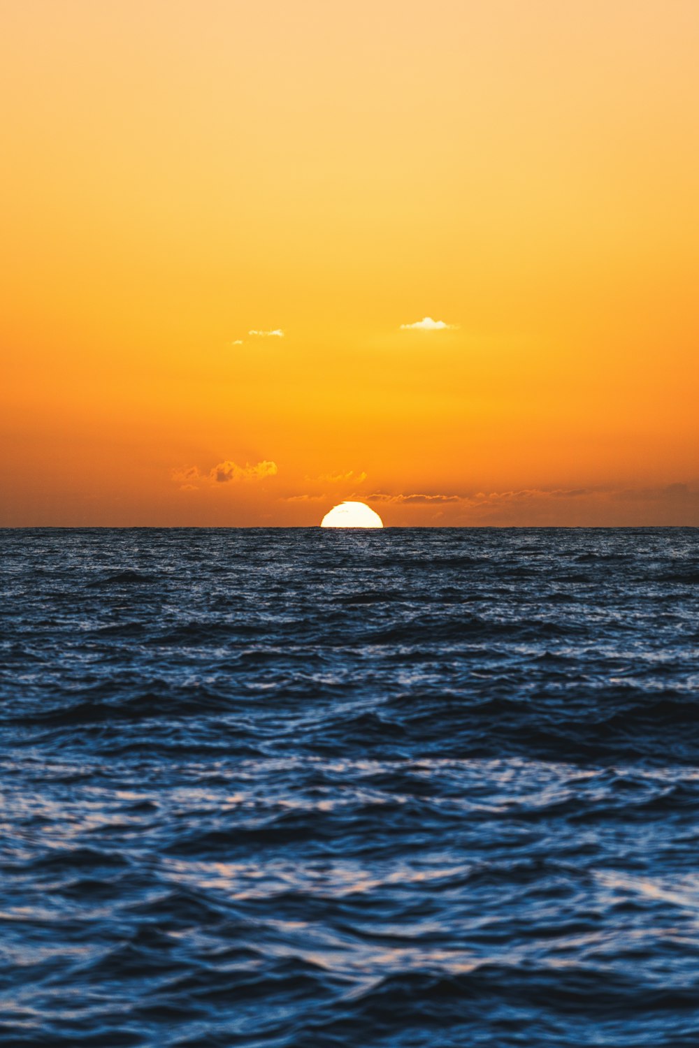 the sun is setting over the ocean with a boat in the distance