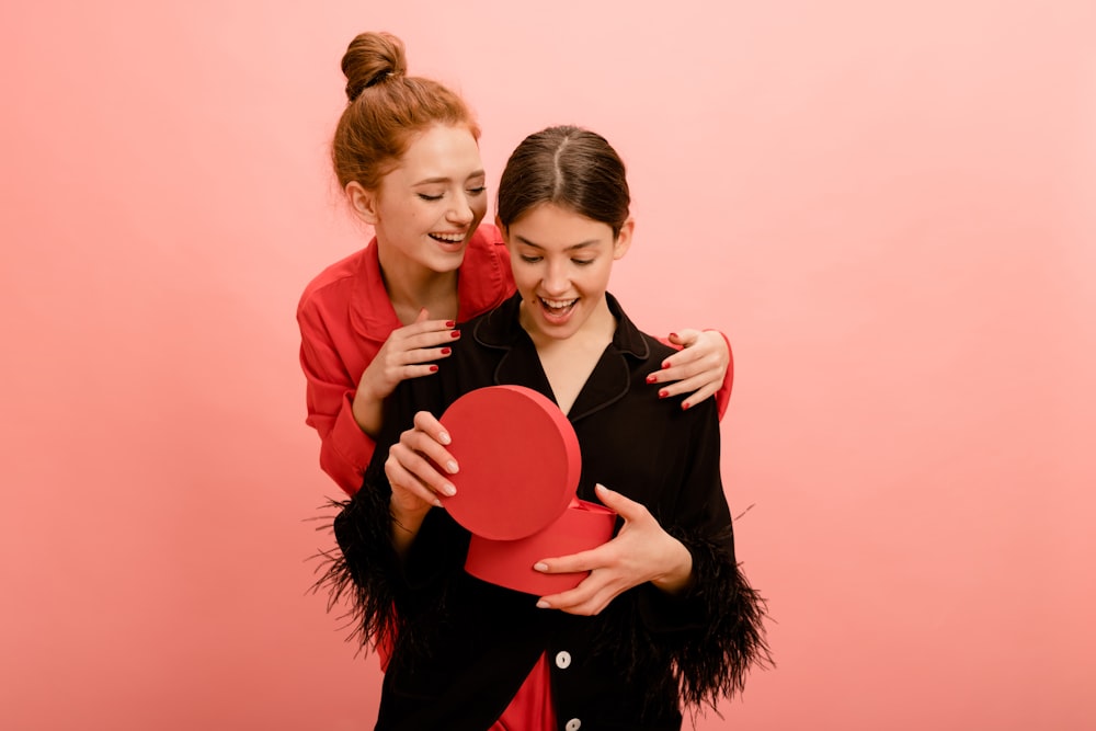 two women hugging each other while holding a red heart