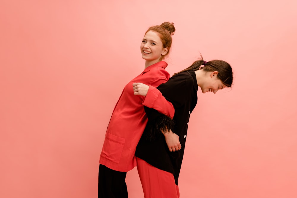 two women standing next to each other in front of a pink wall