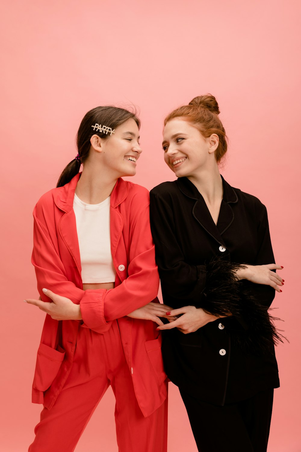 two women standing next to each other in front of a pink background