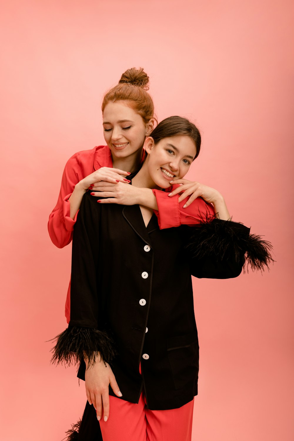 two young women hugging each other in front of a pink background