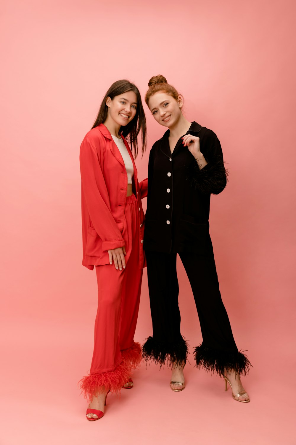 two women standing next to each other in front of a pink background