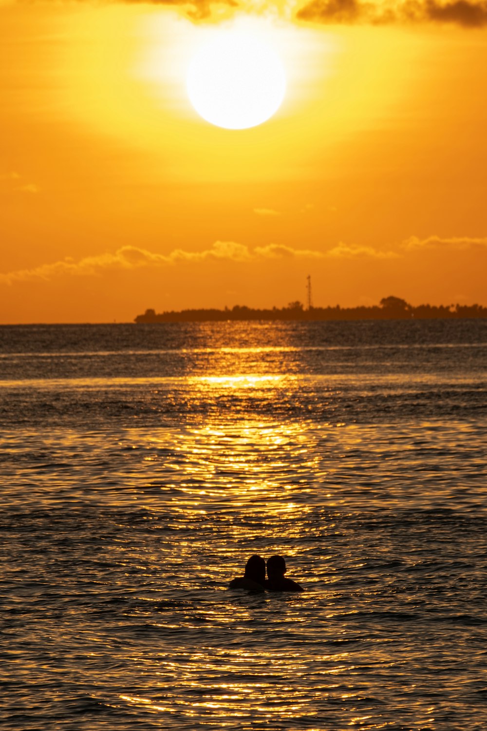 a couple of people swimming in the ocean at sunset