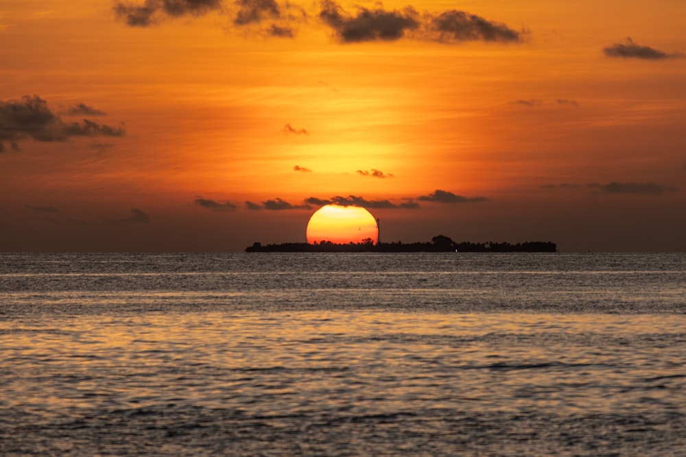 the sun is setting over the ocean with a small island in the distance