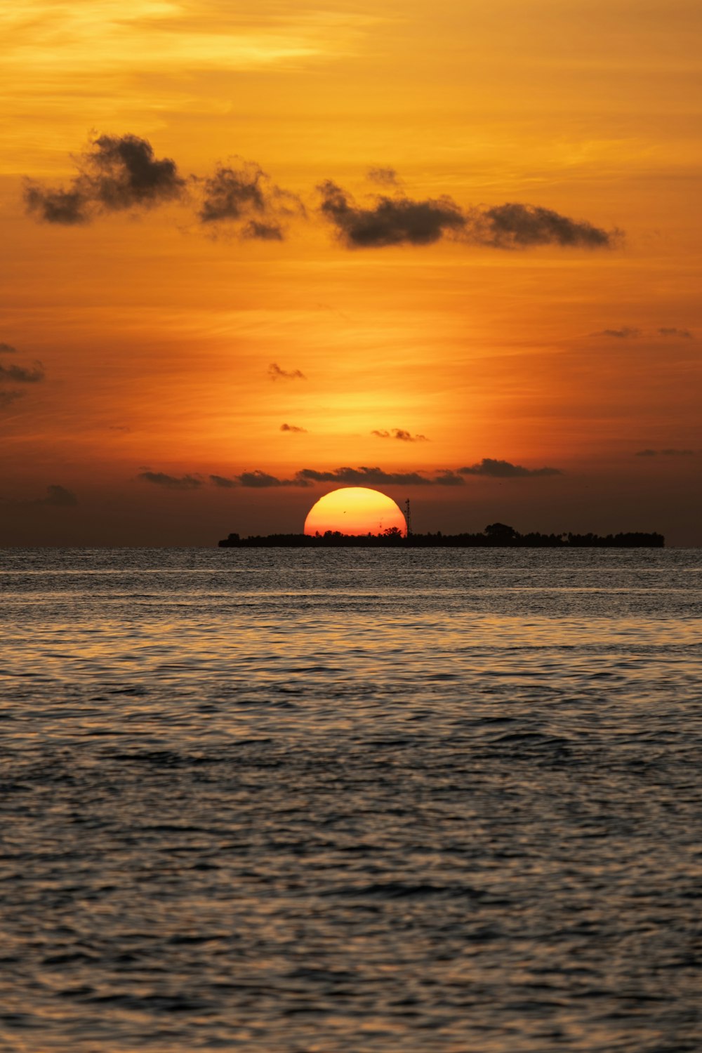 the sun is setting over the ocean with a small island in the distance