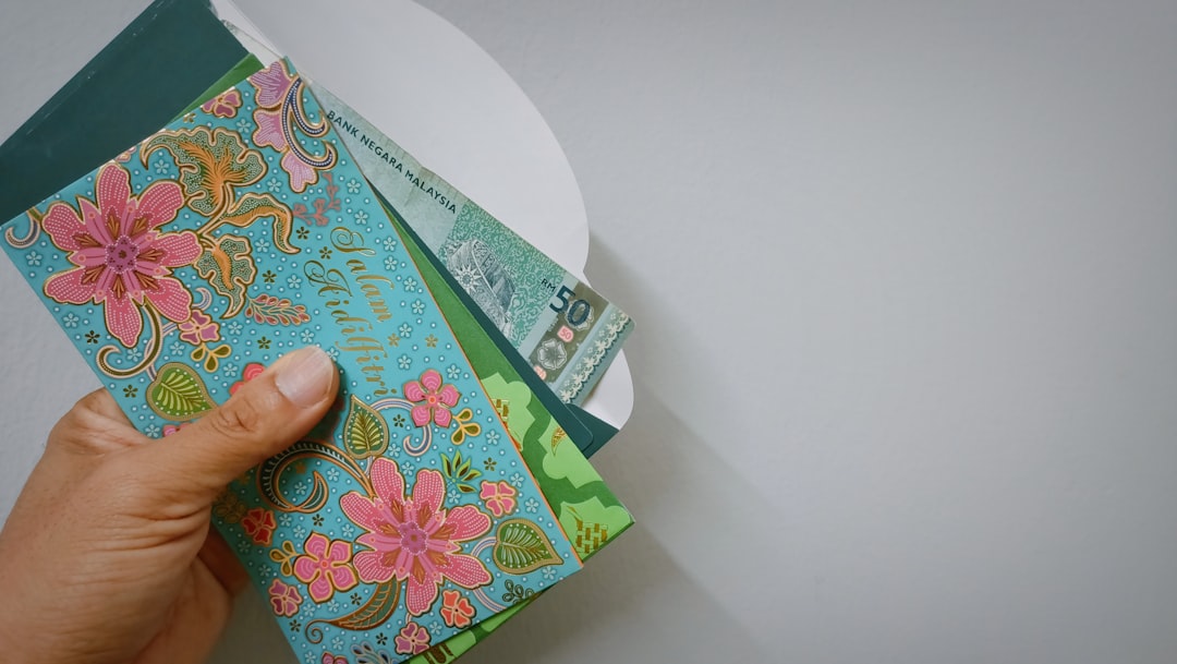 A hand holding a few packets of duit raya