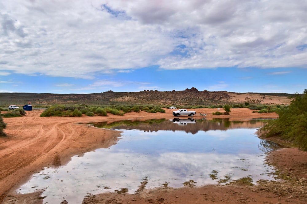 a truck is parked on a dirt road near a body of water