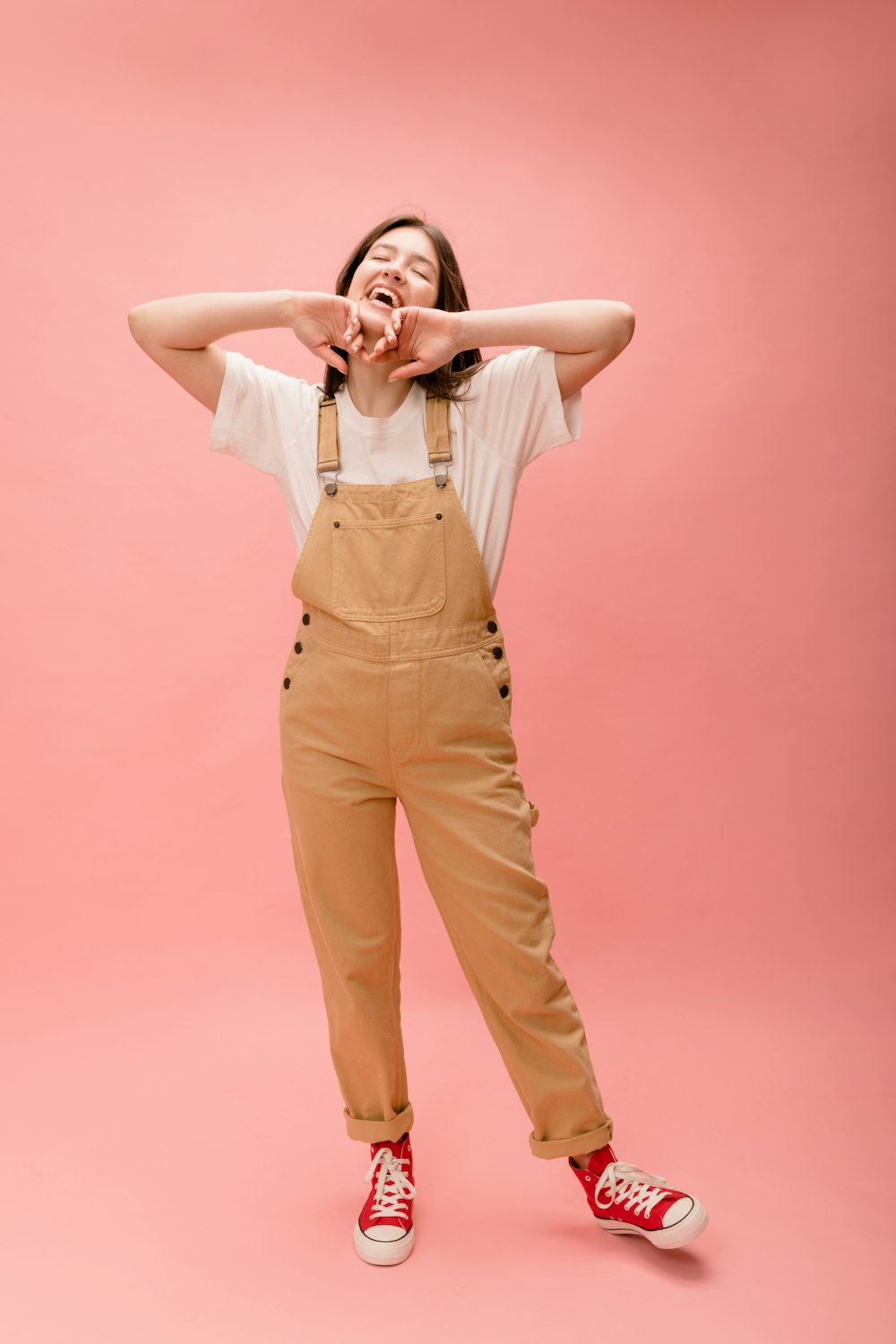 a woman in overalls covers her eyes with her hands