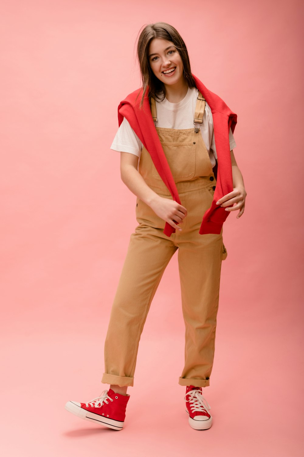 a woman wearing overalls and a red vest