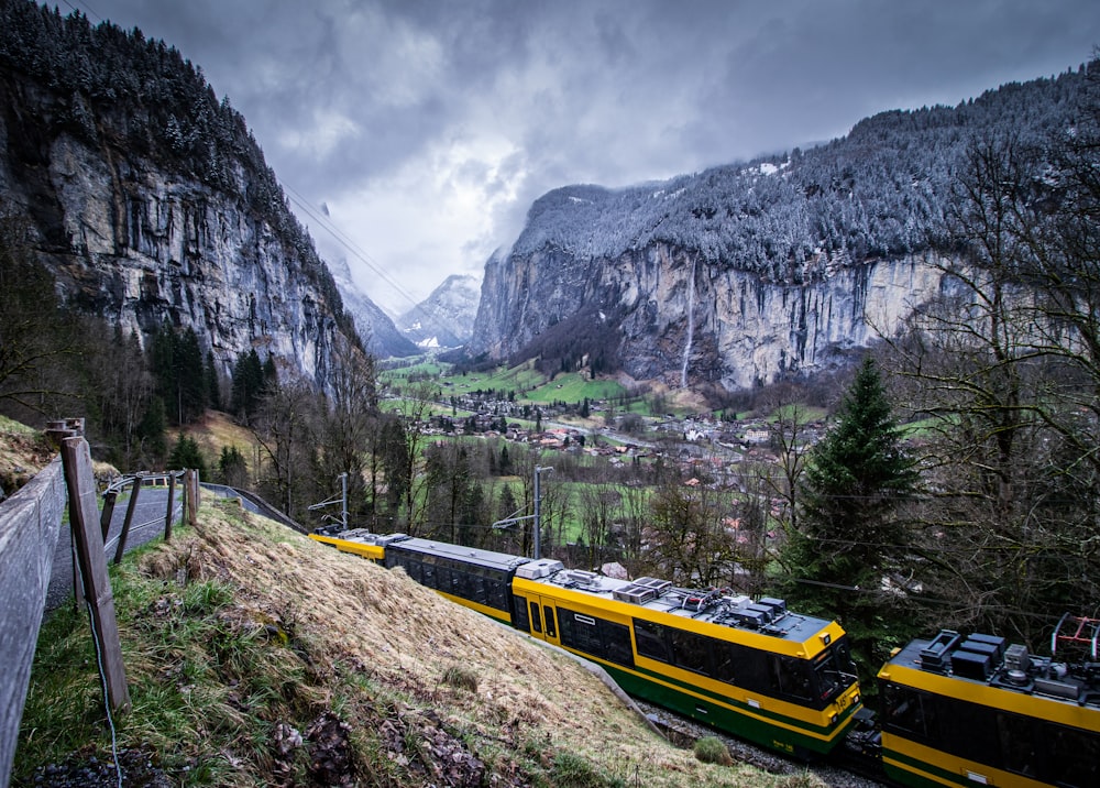 a yellow and black train traveling past a mountain side