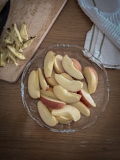 a glass bowl filled with sliced apples on top of a wooden table