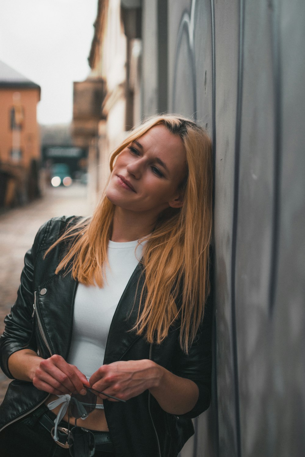 a woman leaning against a wall with her hand on her purse