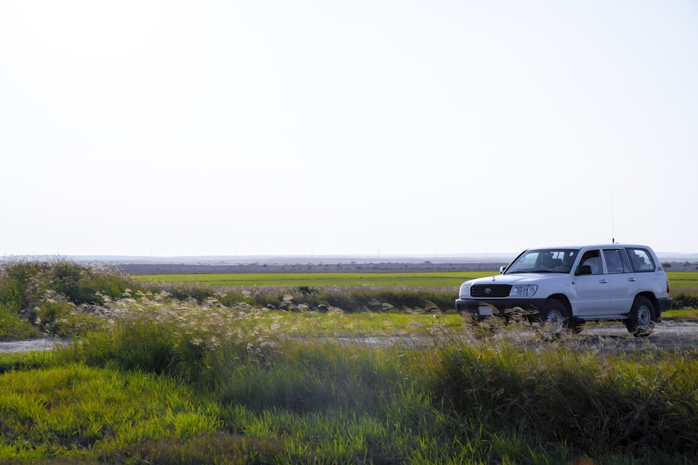 a white suv driving down a road next to a lush green field
