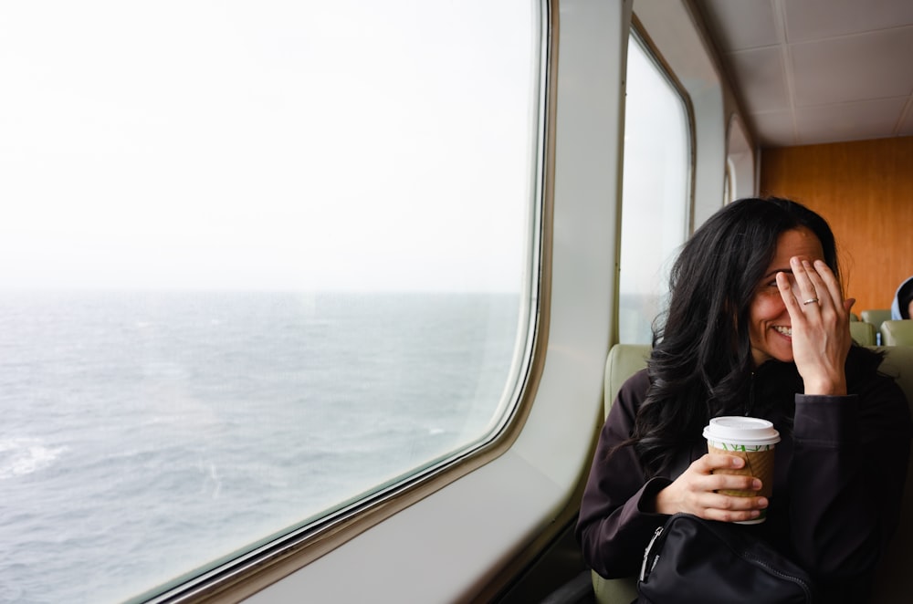 eine Frau sitzt in einem Zug und hält eine Tasse Kaffee in der Hand